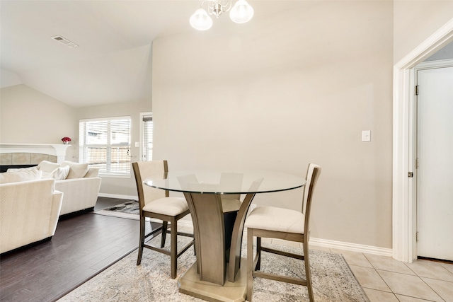 dining room with lofted ceiling, light hardwood / wood-style flooring, a notable chandelier, and a tiled fireplace