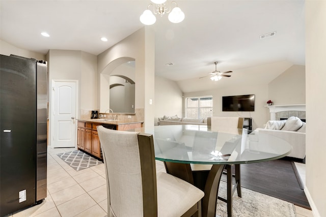 dining space with sink, light tile patterned flooring, a fireplace, ceiling fan with notable chandelier, and lofted ceiling