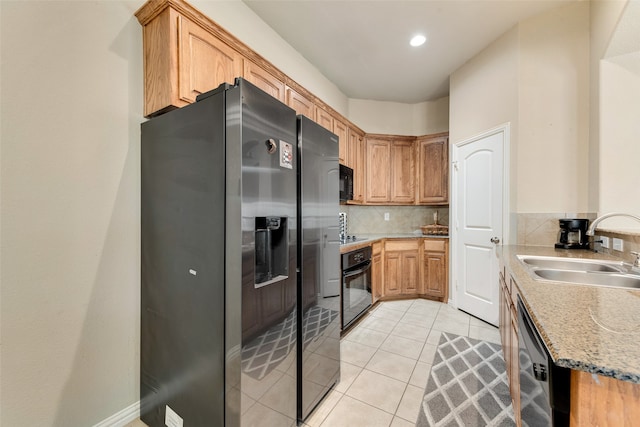 kitchen with decorative backsplash, light tile patterned floors, light stone countertops, black appliances, and sink