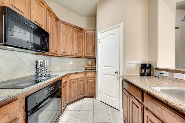 kitchen with light tile patterned flooring, decorative backsplash, light stone countertops, and black appliances