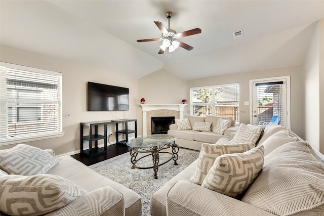 living room with lofted ceiling, hardwood / wood-style floors, a tiled fireplace, and ceiling fan