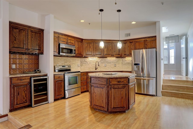 kitchen with a center island, hanging light fixtures, appliances with stainless steel finishes, tasteful backsplash, and beverage cooler