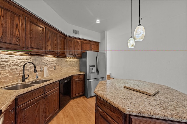 kitchen with light stone countertops, dishwasher, sink, stainless steel fridge, and decorative light fixtures