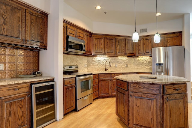 kitchen with sink, beverage cooler, pendant lighting, a kitchen island, and appliances with stainless steel finishes