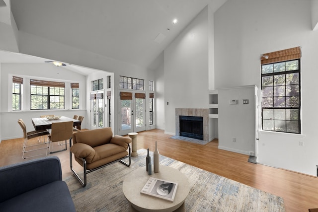 living room featuring a tile fireplace, french doors, high vaulted ceiling, and light wood-type flooring