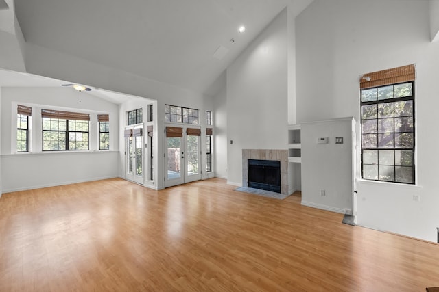 unfurnished living room featuring high vaulted ceiling, french doors, ceiling fan, light wood-type flooring, and a tiled fireplace