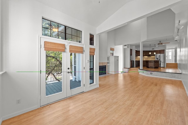 unfurnished living room with ceiling fan, french doors, high vaulted ceiling, and light hardwood / wood-style floors