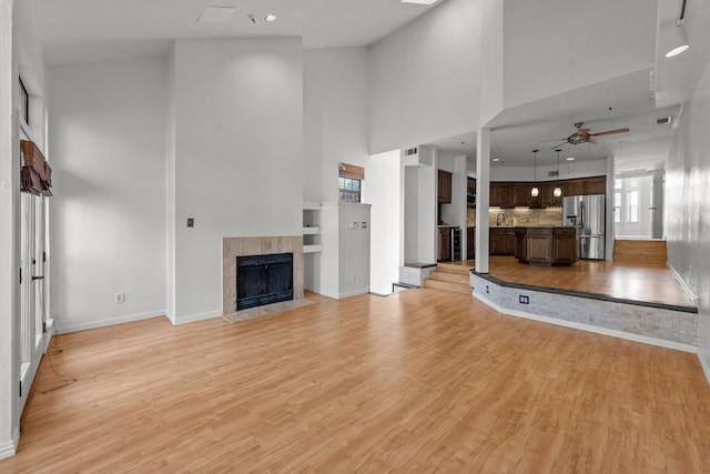 unfurnished living room with a tile fireplace, ceiling fan, light hardwood / wood-style flooring, and a towering ceiling