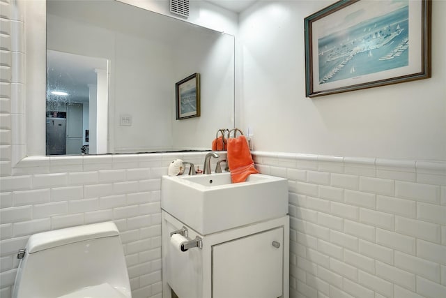 half bath with visible vents, toilet, tile walls, and vanity