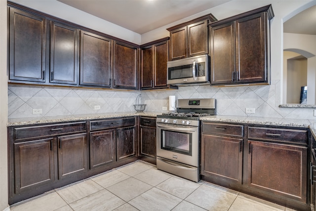 kitchen featuring decorative backsplash, appliances with stainless steel finishes, light stone counters, and dark brown cabinets