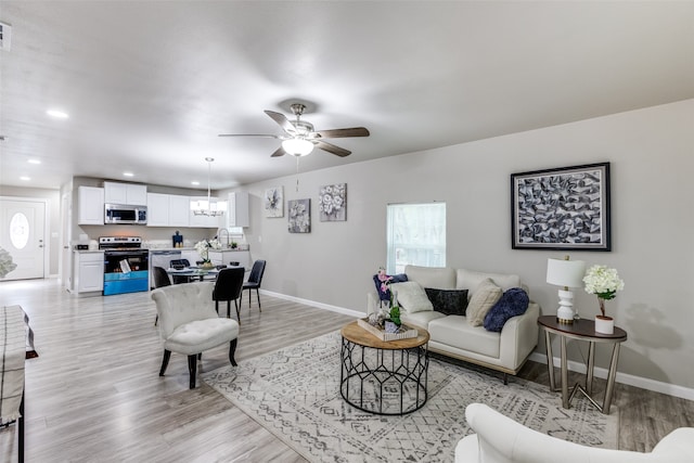 living room featuring light hardwood / wood-style flooring, sink, and ceiling fan with notable chandelier