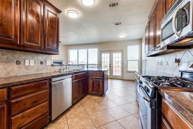 kitchen with appliances with stainless steel finishes, light tile patterned flooring, sink, backsplash, and kitchen peninsula