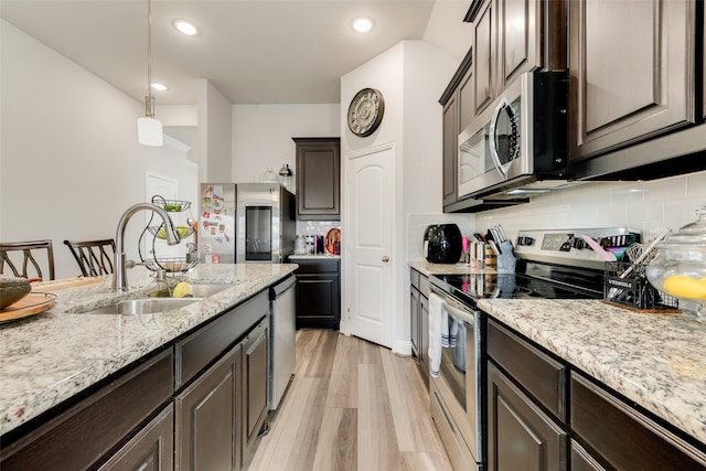 kitchen with appliances with stainless steel finishes, dark brown cabinetry, sink, light hardwood / wood-style flooring, and hanging light fixtures