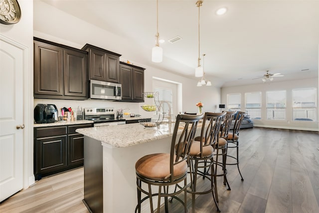 kitchen featuring appliances with stainless steel finishes, light wood-type flooring, pendant lighting, and an island with sink