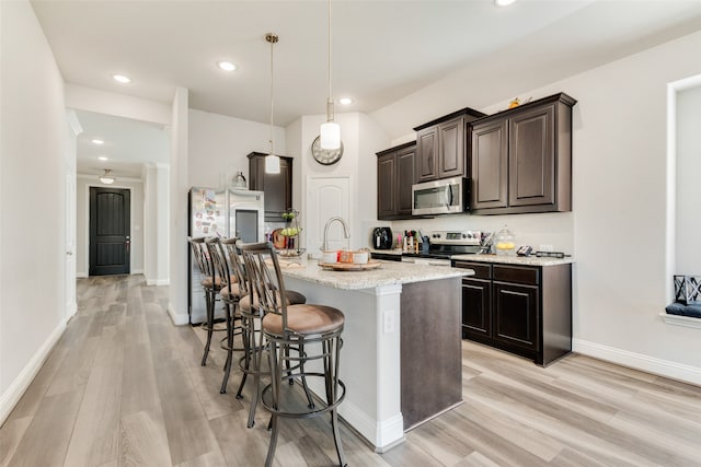 kitchen featuring stainless steel appliances, decorative light fixtures, a kitchen bar, a center island with sink, and light wood-type flooring