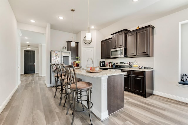 kitchen with appliances with stainless steel finishes, a breakfast bar, hanging light fixtures, a kitchen island with sink, and light stone countertops