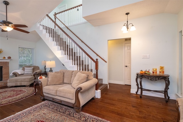 living room featuring dark wood-type flooring, vaulted ceiling, a brick fireplace, and ceiling fan with notable chandelier