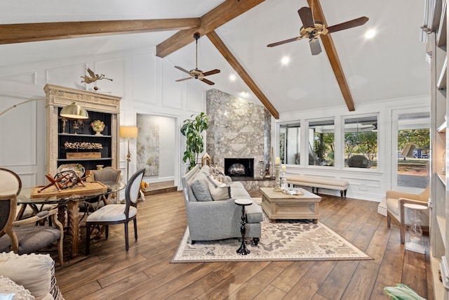 living room with beam ceiling, wood-type flooring, a premium fireplace, high vaulted ceiling, and ceiling fan