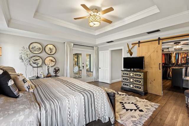 bedroom with crown molding, dark hardwood / wood-style floors, a barn door, and a tray ceiling