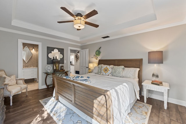 bedroom with dark wood-type flooring, a tray ceiling, crown molding, ensuite bathroom, and ceiling fan