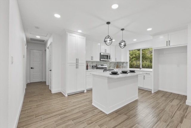 kitchen with white cabinets, appliances with stainless steel finishes, light hardwood / wood-style flooring, and hanging light fixtures