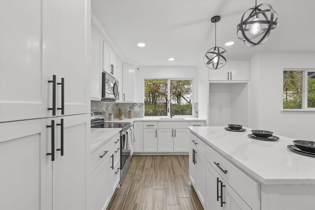 kitchen featuring a wealth of natural light, white cabinetry, hanging light fixtures, and appliances with stainless steel finishes