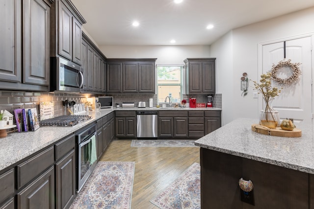 kitchen featuring dark brown cabinets, stainless steel appliances, sink, light hardwood / wood-style floors, and tasteful backsplash