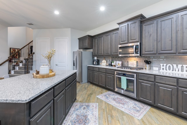 kitchen with a kitchen island, stainless steel appliances, light stone counters, light hardwood / wood-style floors, and tasteful backsplash