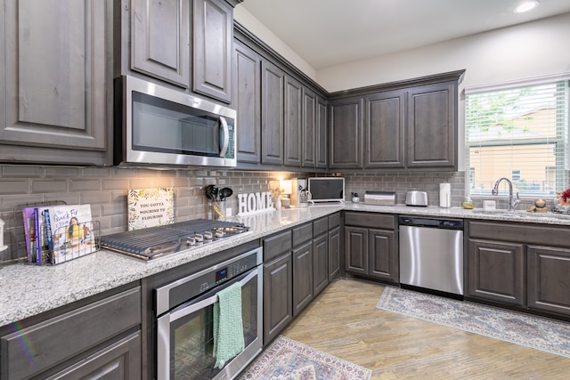 kitchen with backsplash, appliances with stainless steel finishes, light wood-type flooring, dark brown cabinetry, and sink