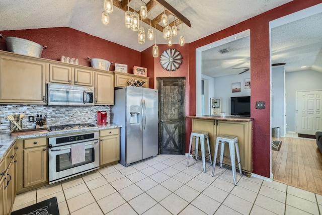 kitchen featuring appliances with stainless steel finishes, a textured ceiling, hanging light fixtures, ceiling fan, and vaulted ceiling