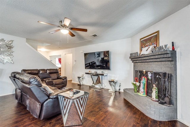 living room with dark wood-type flooring, a brick fireplace, a textured ceiling, and ceiling fan