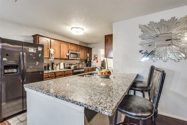 kitchen with light stone countertops, sink, a textured ceiling, stainless steel appliances, and a breakfast bar area