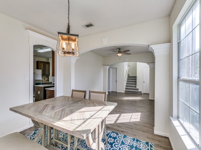 dining space with dark hardwood / wood-style floors, ceiling fan with notable chandelier, plenty of natural light, and decorative columns