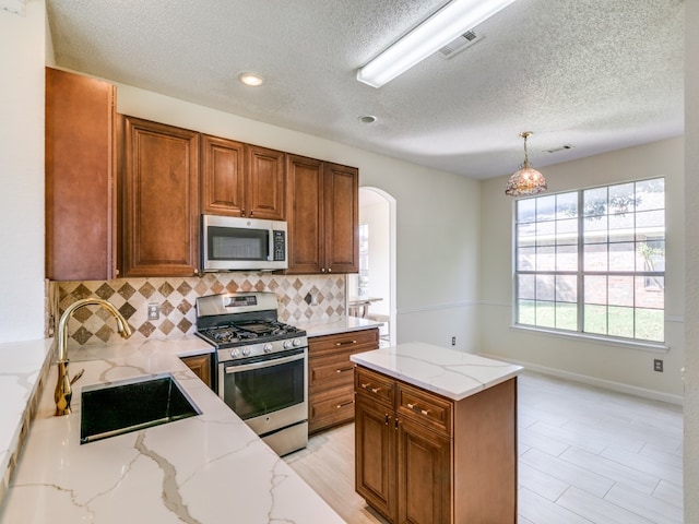 kitchen with sink, stainless steel appliances, decorative light fixtures, light stone counters, and decorative backsplash