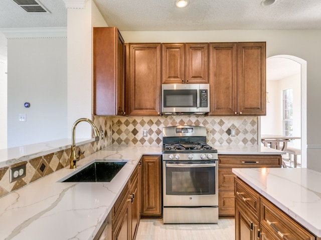 kitchen featuring decorative backsplash, a textured ceiling, light stone countertops, sink, and stainless steel appliances