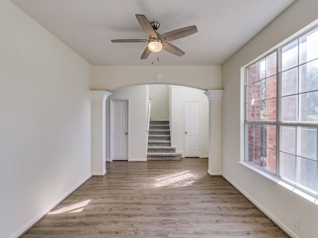 spare room featuring a textured ceiling, hardwood / wood-style flooring, ceiling fan, and decorative columns