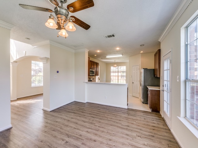 unfurnished living room with ceiling fan, a textured ceiling, light wood-type flooring, decorative columns, and ornamental molding