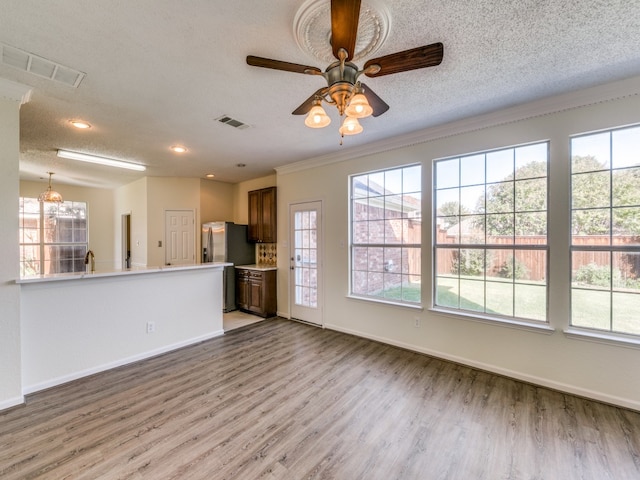 unfurnished living room with crown molding, hardwood / wood-style floors, a textured ceiling, and ceiling fan with notable chandelier