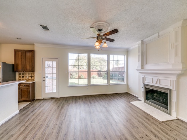 unfurnished living room featuring ornamental molding, light hardwood / wood-style flooring, a textured ceiling, and ceiling fan