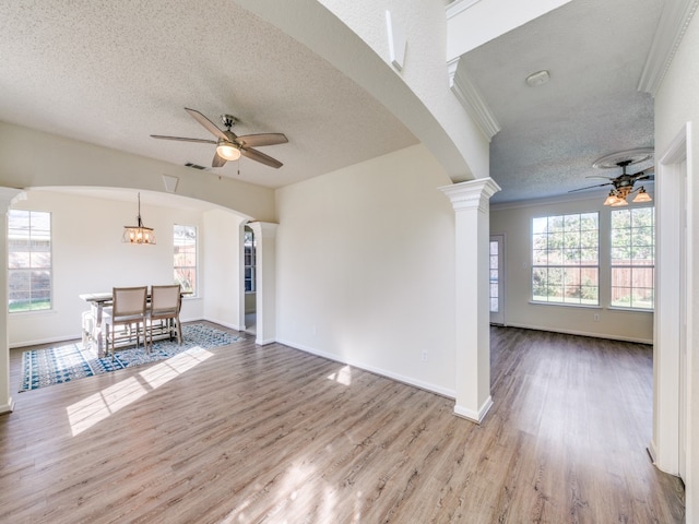 unfurnished living room with a textured ceiling, decorative columns, ornamental molding, ceiling fan with notable chandelier, and light hardwood / wood-style floors