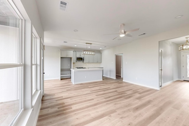 unfurnished living room featuring sink, ceiling fan with notable chandelier, and light wood-type flooring