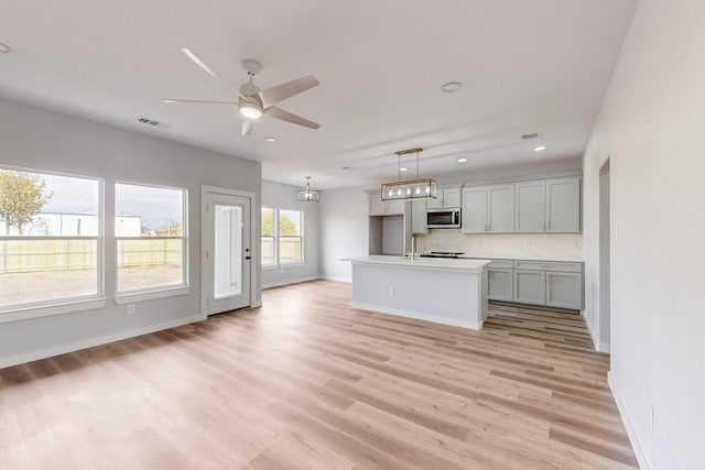 kitchen featuring an island with sink, light hardwood / wood-style flooring, ceiling fan with notable chandelier, gray cabinetry, and pendant lighting