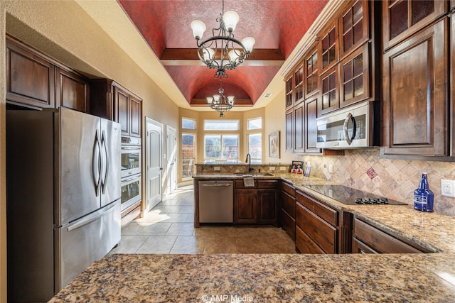 kitchen with appliances with stainless steel finishes, vaulted ceiling, pendant lighting, light tile patterned floors, and an inviting chandelier