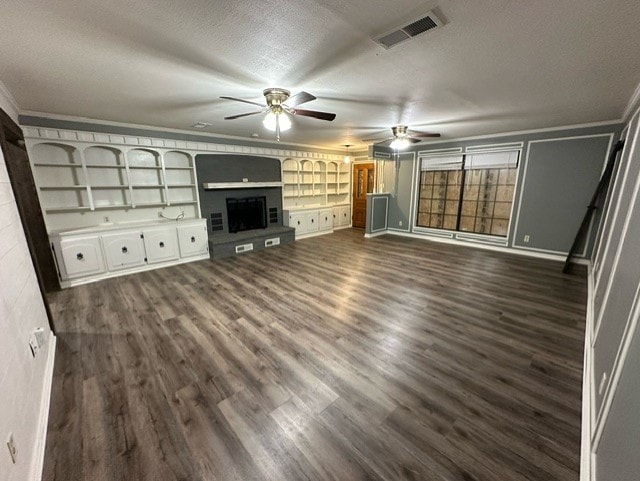 unfurnished living room featuring built in shelves, ceiling fan, dark wood-type flooring, a textured ceiling, and ornamental molding