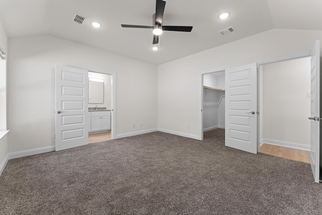 unfurnished bedroom featuring a walk in closet, a closet, ceiling fan, vaulted ceiling, and dark carpet