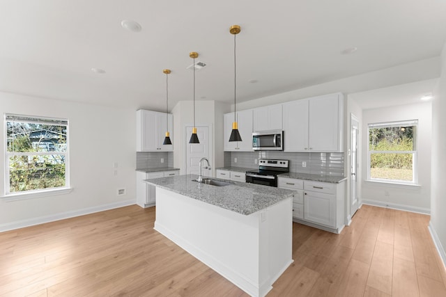 kitchen with light hardwood / wood-style flooring, light stone countertops, white cabinets, decorative light fixtures, and appliances with stainless steel finishes