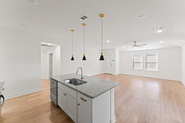 kitchen with light hardwood / wood-style flooring, an island with sink, sink, light stone countertops, and decorative light fixtures