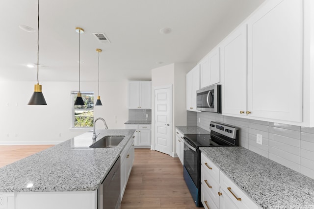 kitchen with a center island with sink, appliances with stainless steel finishes, decorative light fixtures, and white cabinets