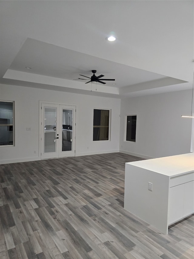 unfurnished living room with french doors, light hardwood / wood-style flooring, ceiling fan, and a raised ceiling