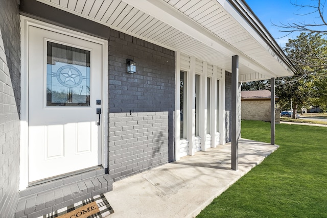 view of exterior entry featuring a yard and a porch